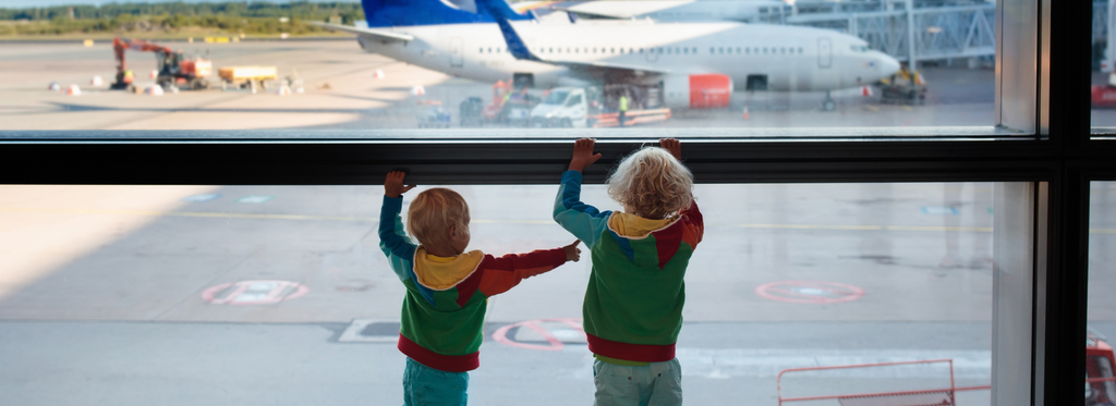 Two children watching airplanes from the airport terminal window.